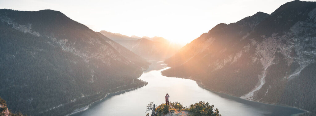Ein Wanderer steht oberhalb von einem Bergsee.